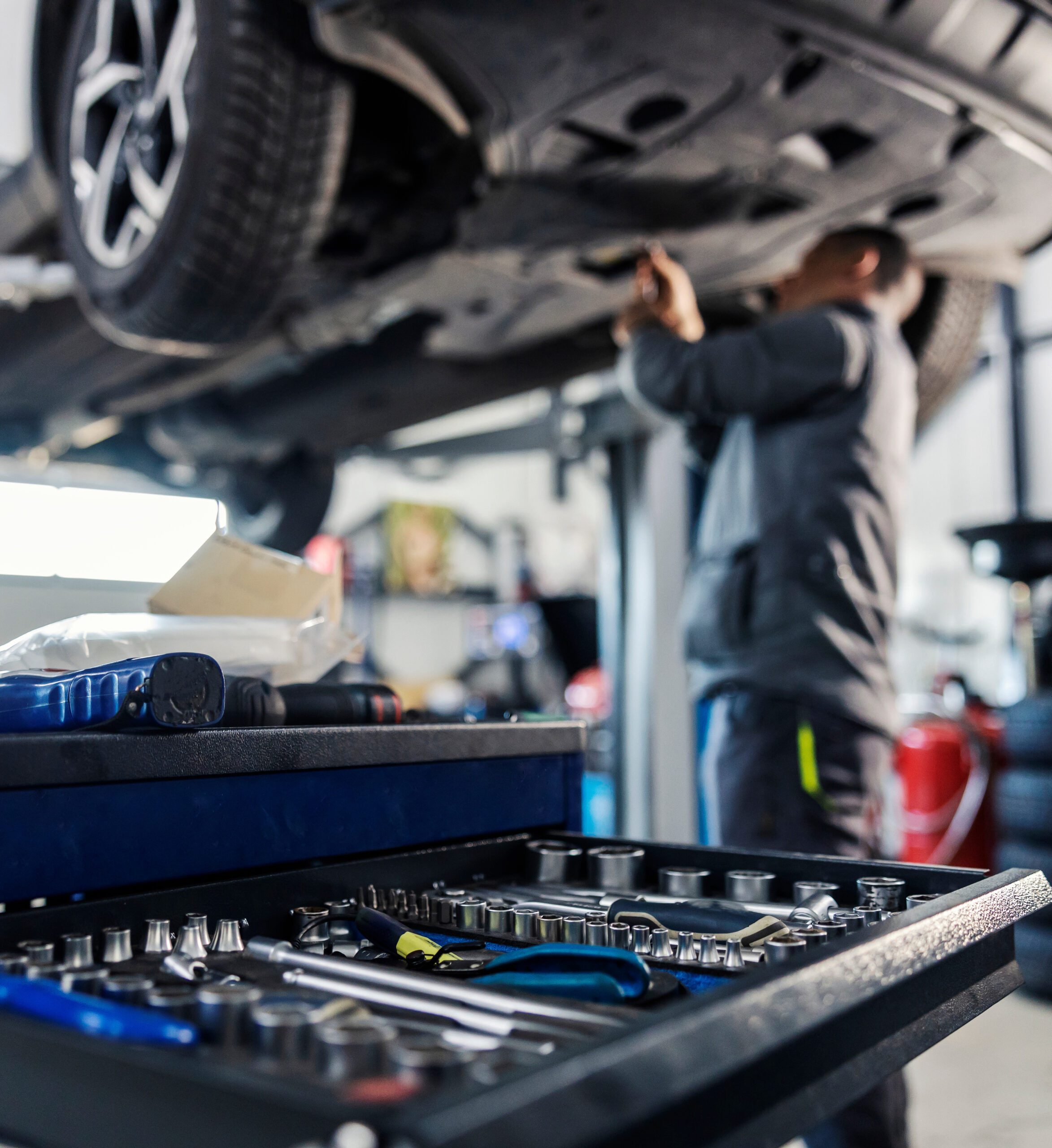 Selective focus on a tools in toolbox at mechanic's shop with mechanic repairing the car in blurry background. reparation et entretien vehicule à colomiers